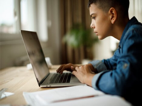 پسر نوجوانی نشسته پشت میز در حال جست و جوی هزینه کلاس در لپ تاپ