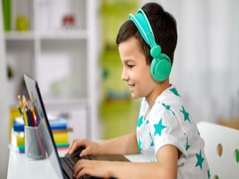 عکس کودک پسری که پشت میز نشسته است و با لپ تاپ خود در کلاس آنلاین حضور دارد.